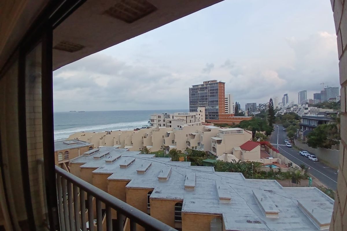 Elevated coastal view overlooking surrounding apartment complexes, urban streets, and the ocean horizon from a balcony.