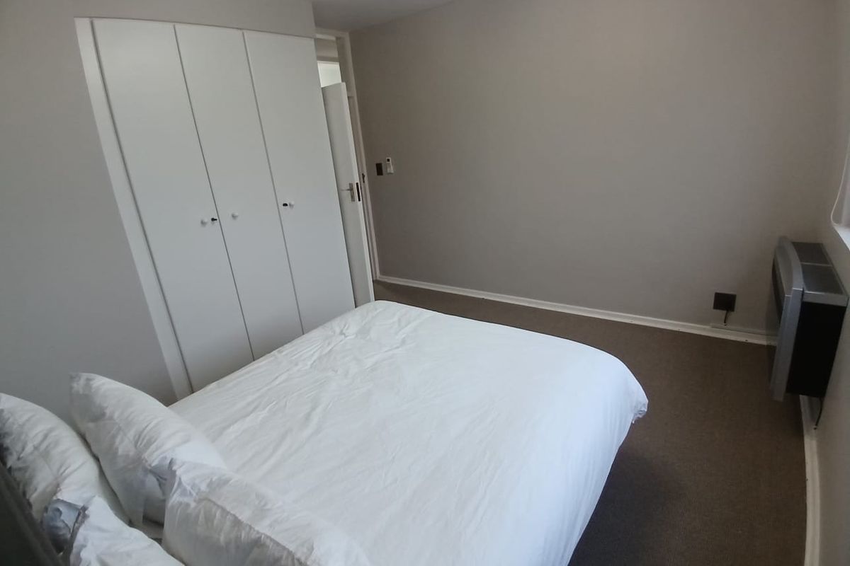 A functional bedroom featuring neutral wall tones, carpeted flooring, and a built-in wardrobe for storage.