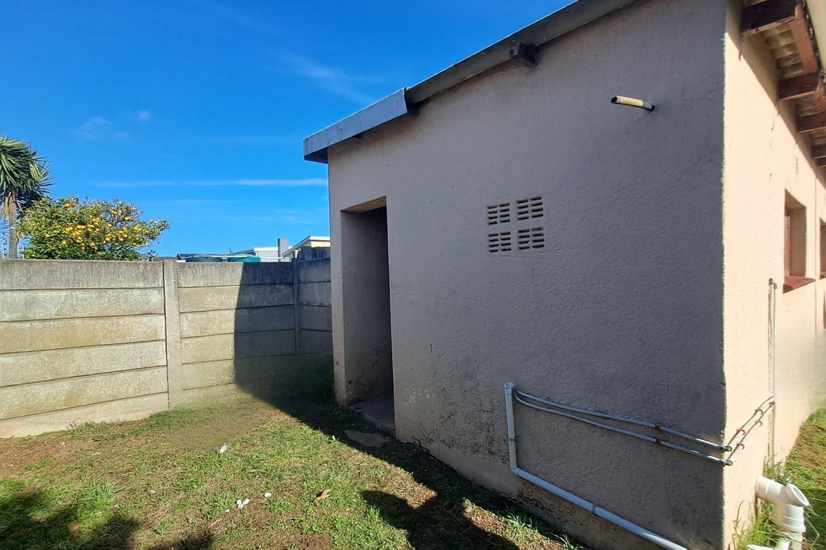 Rear exterior view of the property showing a precast concrete boundary wall, exposed plumbing, and a side entrance to the building.