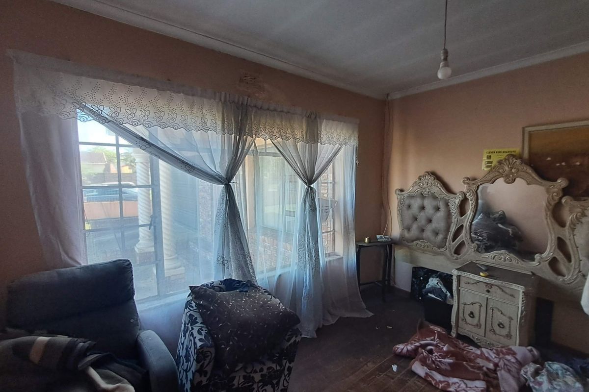 A bedroom featuring a large window with natural light, coved ceilings, and visible signs of wear on the ceiling and flooring.