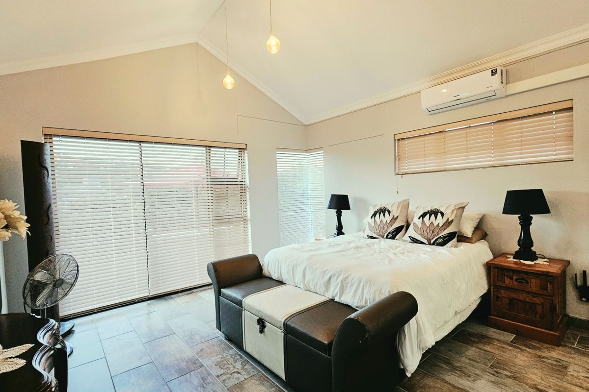 Spacious bedroom featuring a vaulted ceiling, tiled flooring, split-system air conditioning, and large windows with venetian blinds for natural light control.