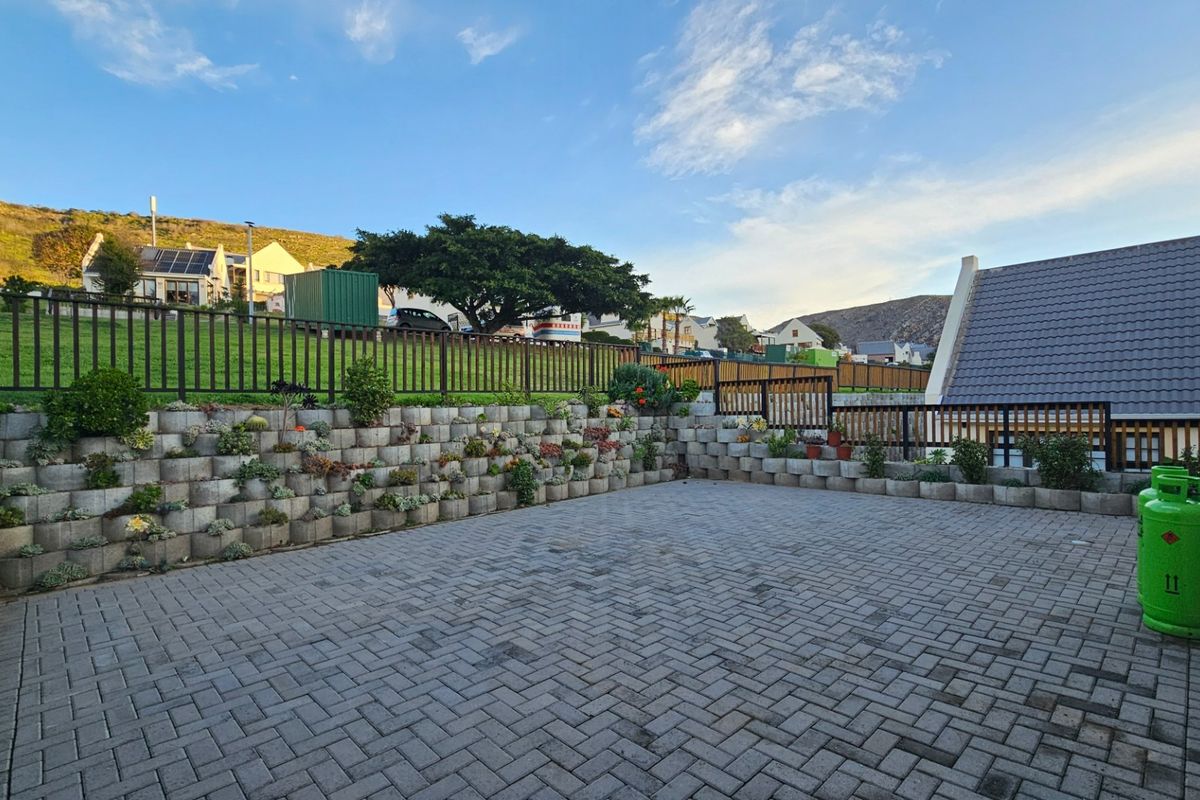 A spacious paved rear courtyard featuring tiered retaining walls with integrated planting and secure perimeter fencing.