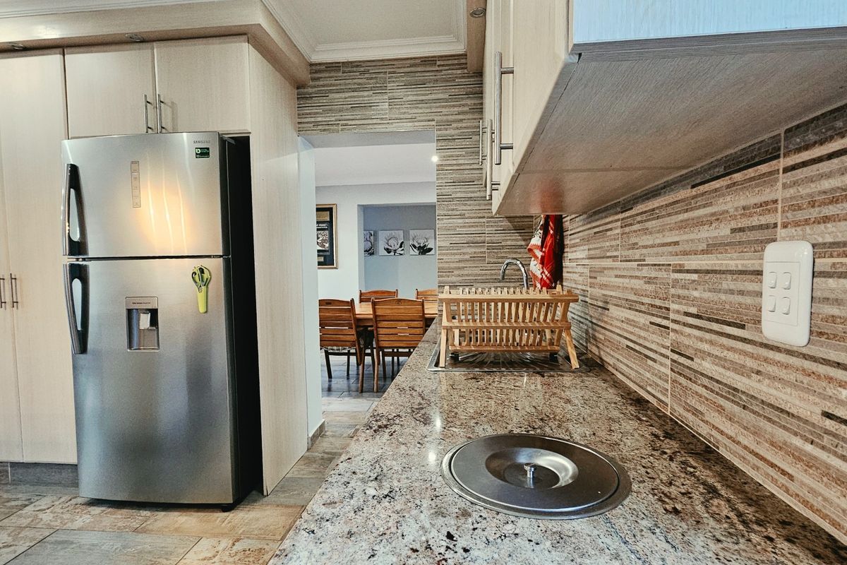 A functional kitchen featuring granite countertops, tiled backsplash, and ample built-in cabinetry, with a view through to the adjacent dining area.