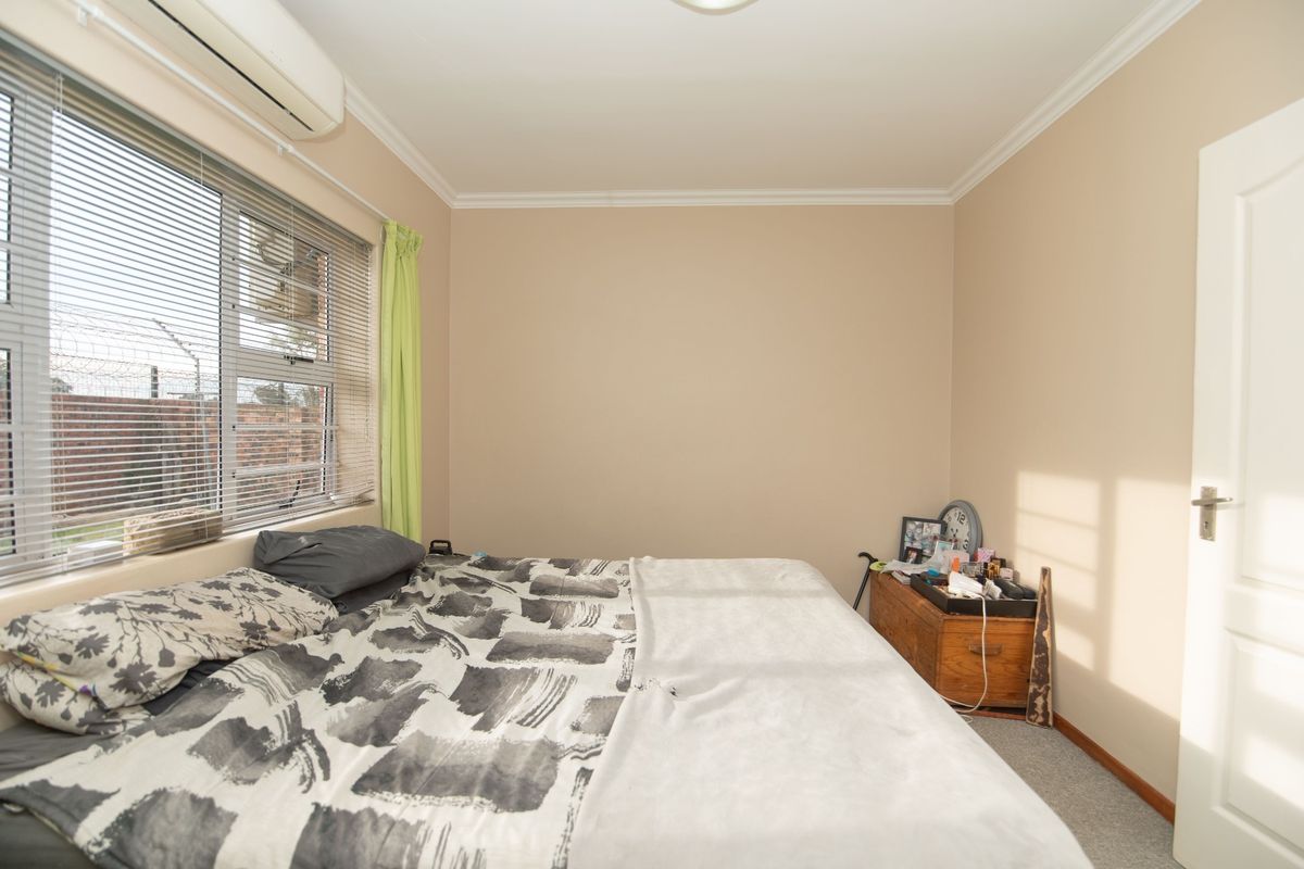 A functional bedroom featuring neutral wall tones, carpet flooring, and a wall-mounted split-system air conditioning unit.