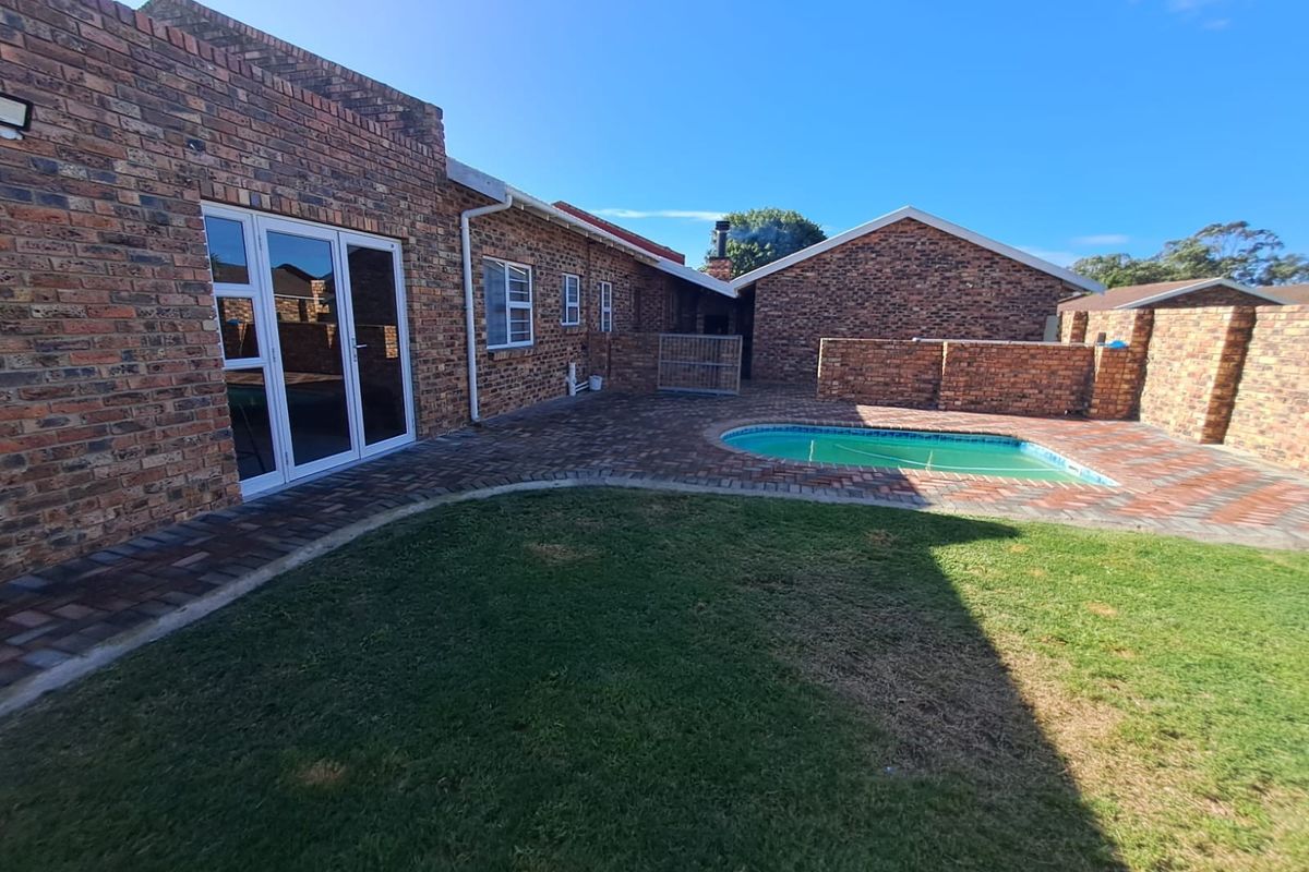 Rear exterior view of the townhouse featuring a private swimming pool, paved patio area, and a well-maintained lawn enclosed by brick boundary walls.