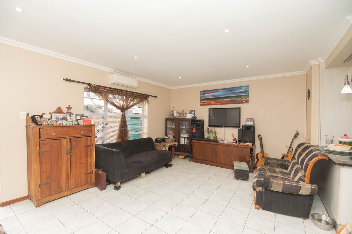 A spacious living room featuring tiled flooring, recessed downlighting, and a wall-mounted split-system air conditioning unit.