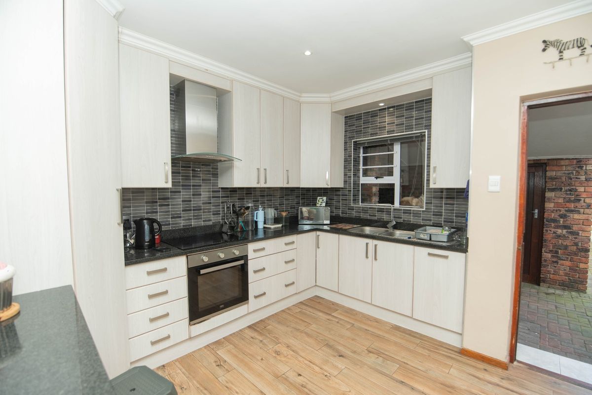 Modern kitchen featuring light wood-grain cabinetry, dark granite countertops, a stainless steel extractor fan, built-in oven, and a stylish tiled backsplash.