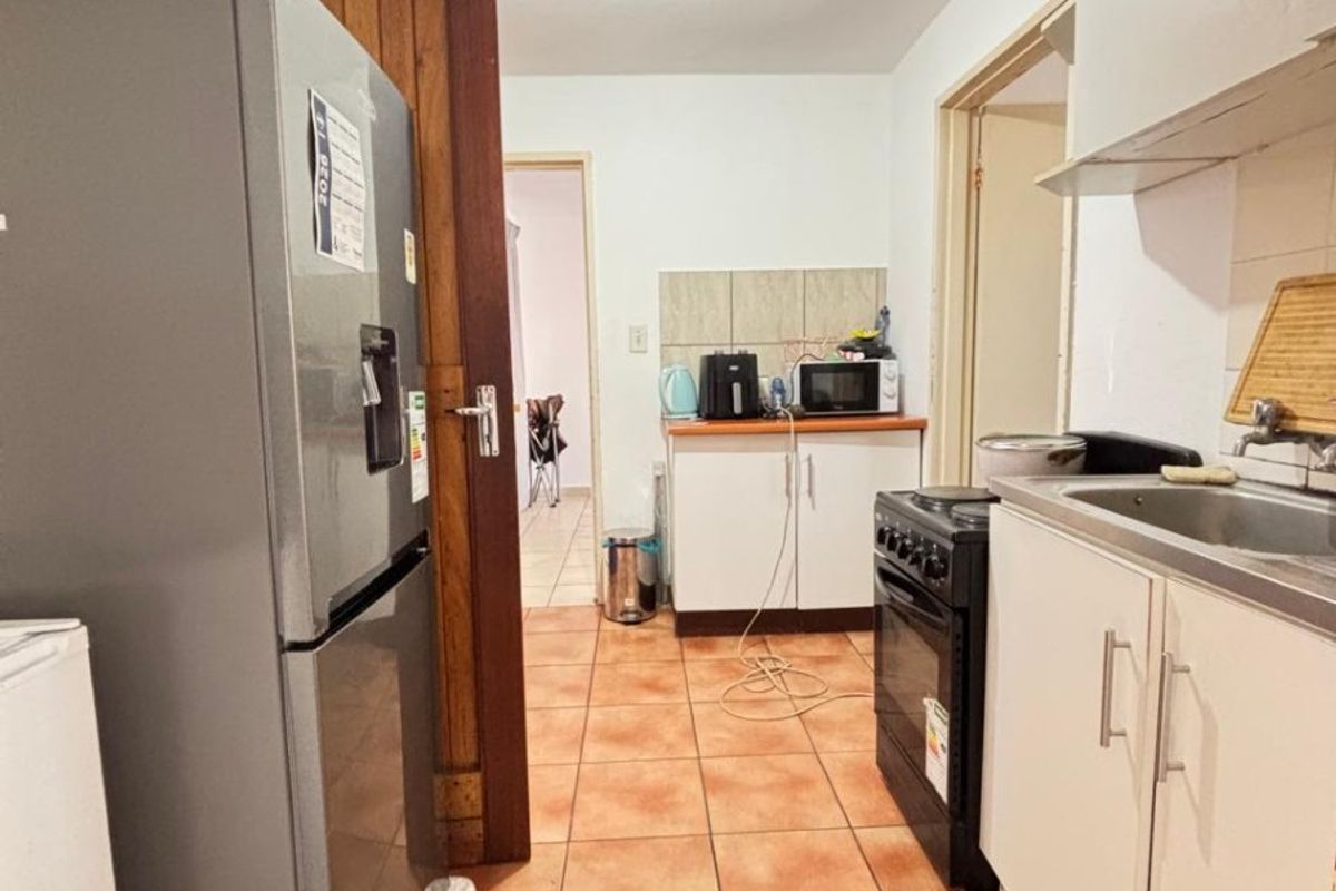 A functional kitchen featuring tiled flooring, built-in cabinetry, a stainless steel sink, and a freestanding stove, offering a practical layout for daily use.