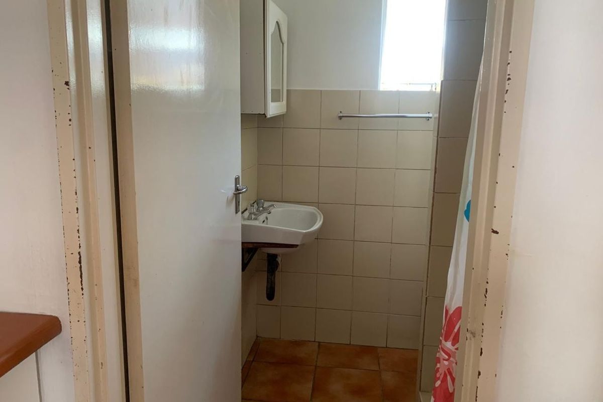 A compact bathroom featuring a wall-mounted basin, tiled walls and flooring, and a medicine cabinet, requiring cosmetic updates to improve its overall condition.