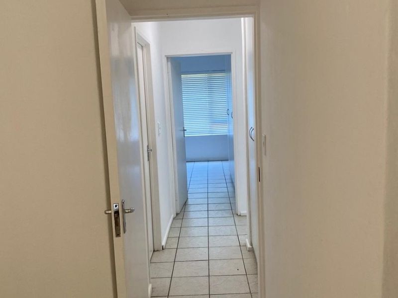 A functional hallway featuring tiled flooring and multiple internal doors, leading towards a bright room with window blinds.