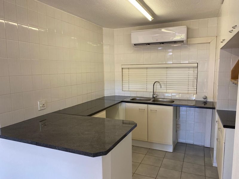 A functional kitchen featuring dark laminate countertops, tiled backsplash, double sink, and a wall-mounted air conditioning unit.