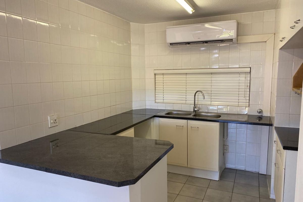 A functional kitchen featuring dark laminate countertops, tiled backsplash, double sink, and a wall-mounted air conditioning unit.