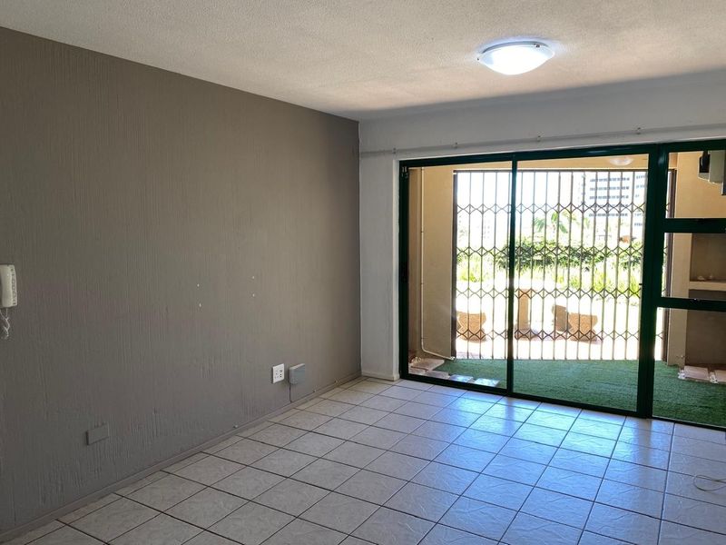 An empty living room featuring tiled flooring, a sliding glass door with a security gate, and direct access to an outdoor patio area.