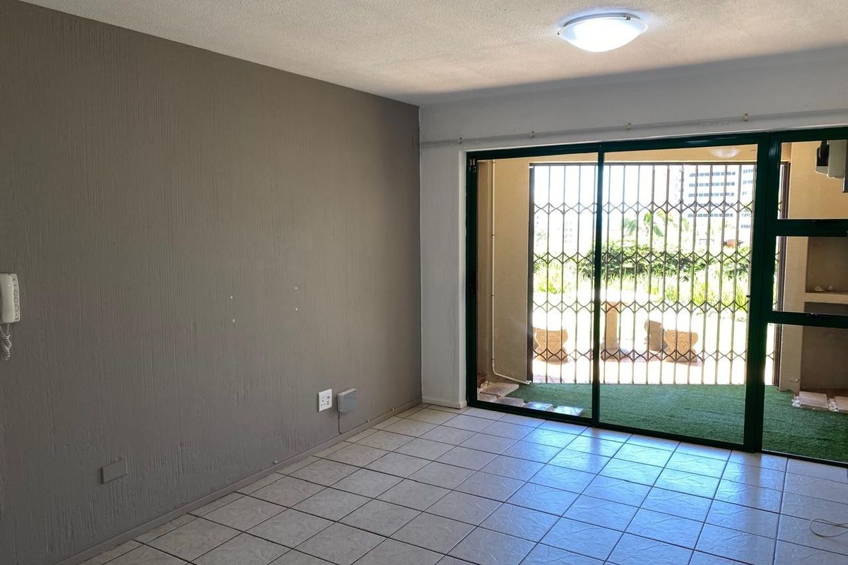 An empty living room featuring tiled flooring, a sliding glass door with a security gate, and direct access to an outdoor patio area.