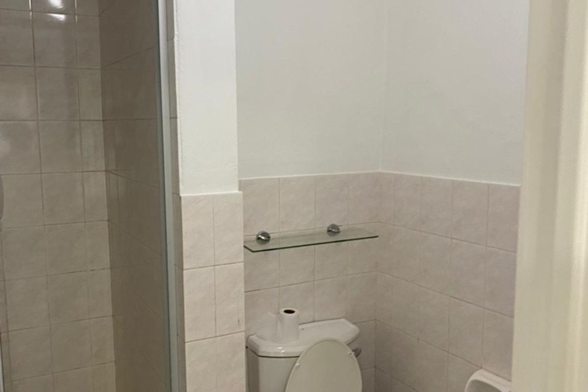 A functional bathroom featuring a shower enclosure, toilet, and tiled wall finishes with an integrated extractor fan.