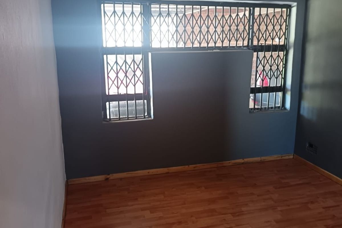 An empty bedroom featuring laminate flooring, recessed downlights, and a window fitted with a security gate.