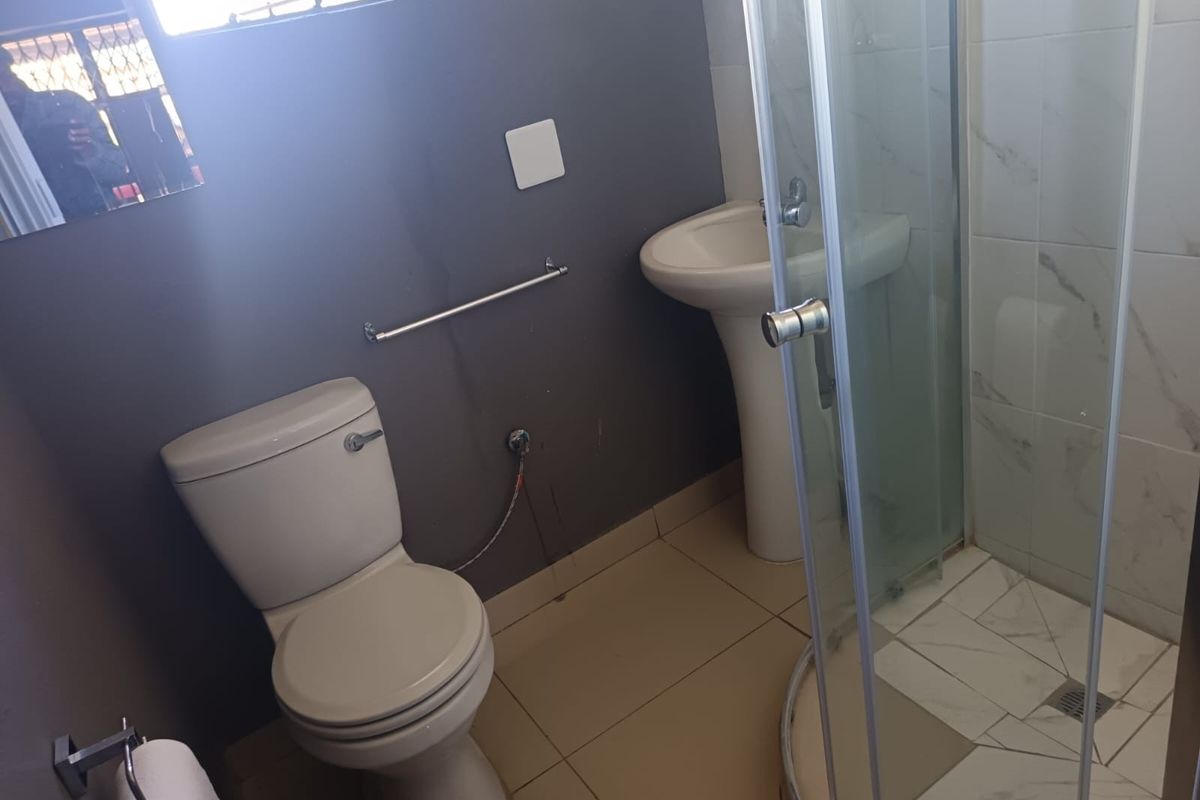 A functional bathroom featuring a pedestal basin, toilet, and a glass-enclosed shower with tiled flooring and neutral wall finishes.