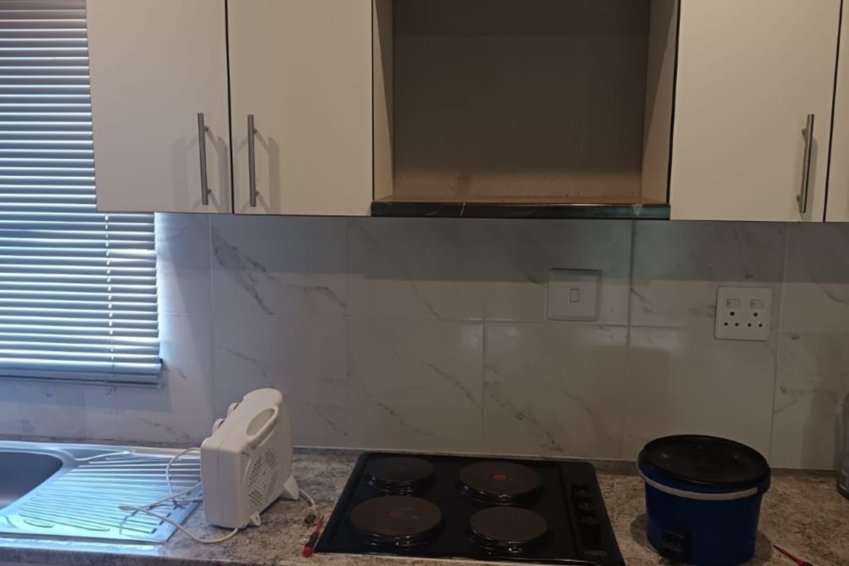 A functional kitchen featuring white cabinetry, a four-plate electric hob, marble-look splashback tiling, and a stainless steel sink with integrated drainer.