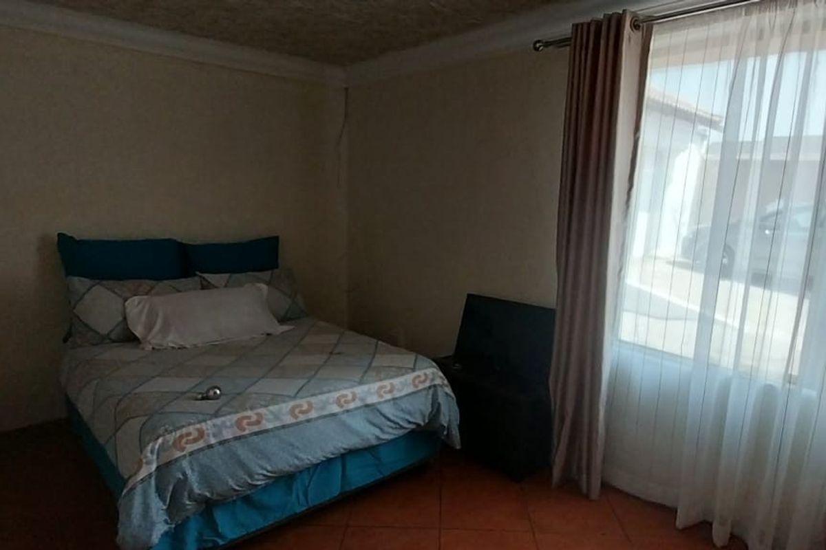 A bedroom featuring tiled flooring and large windows with curtain rails, providing natural light.