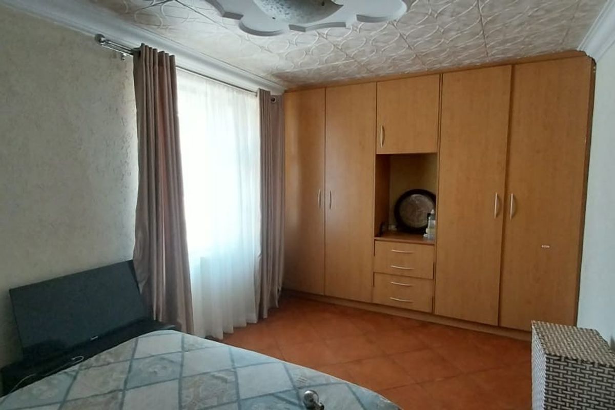 A bedroom featuring built-in wooden wardrobes, tiled flooring, and decorative ceiling tiles, offering a functional space with potential for modern updates.