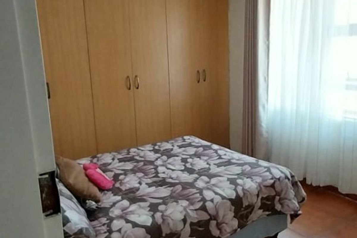 A bedroom featuring built-in wooden cupboards, terracotta-style floor tiles, and a decorative ceiling rose with textured ceiling panels.