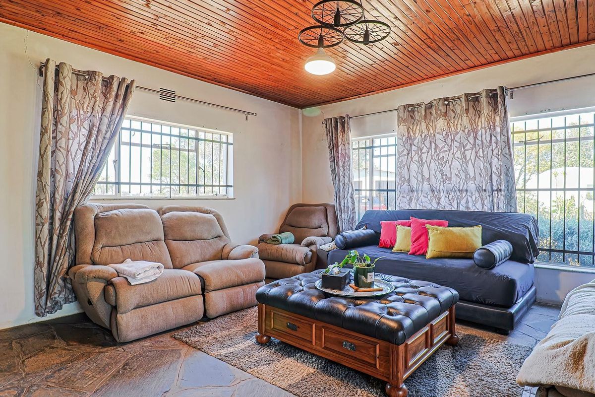 A living room featuring a warm timber tongue and groove ceiling, rustic flagstone flooring, and windows fitted with security bars.
