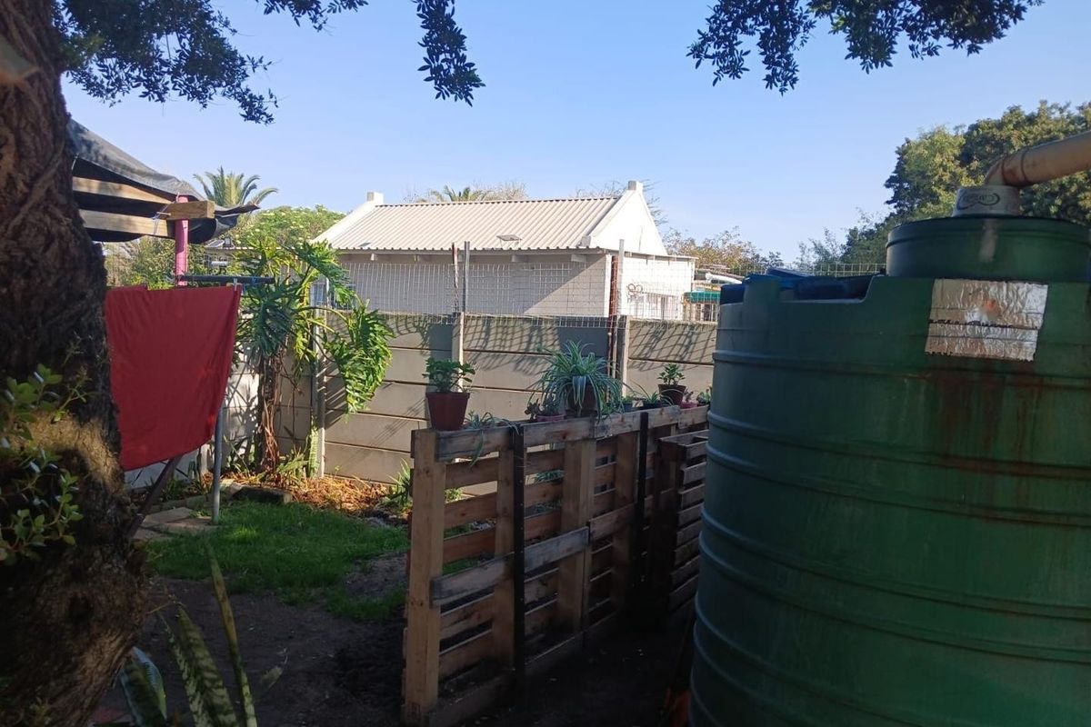Rear garden area featuring a large green water storage tank, precast concrete boundary walling, and established trees.