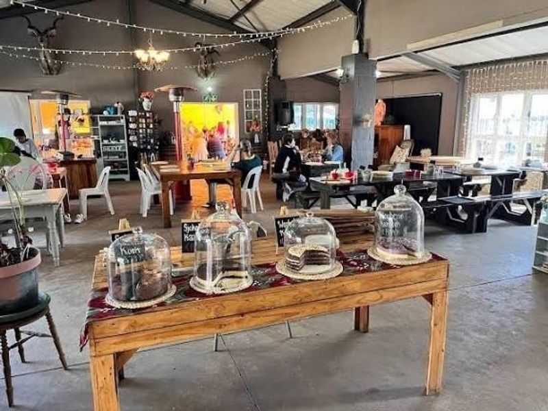 Spacious open-plan farm venue featuring exposed steel roof trusses, concrete flooring, and large windows, currently utilized as a dining and social space.