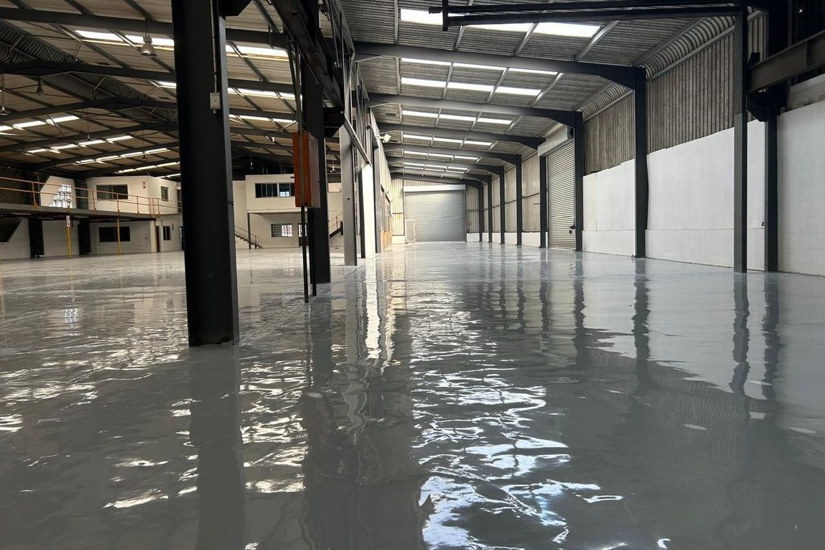 Spacious industrial warehouse featuring a high-gloss epoxy floor, steel portal frame construction, integrated mezzanine level, and ample natural light through roof skylights.