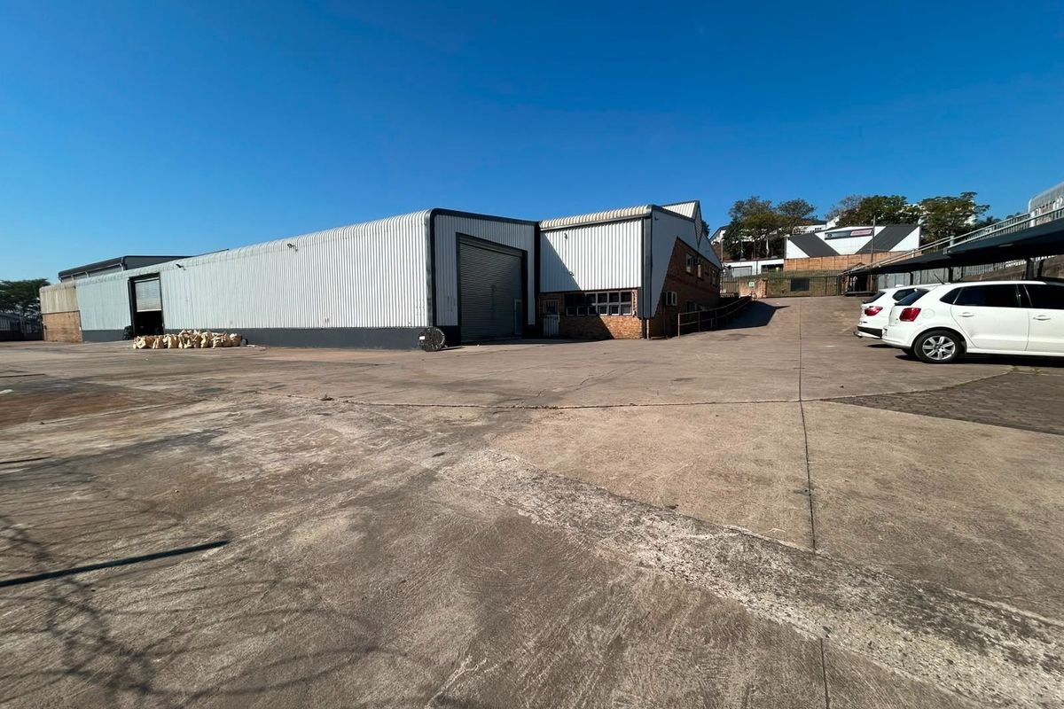 Rear exterior view of a commercial warehouse facility featuring corrugated metal cladding, roller shutter access doors, and a large concrete yard area.