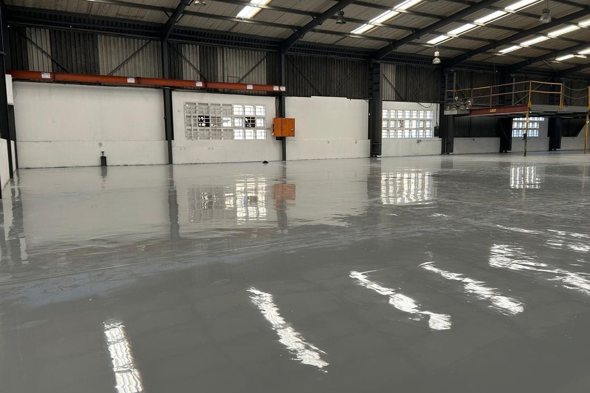 Spacious industrial warehouse featuring a high-gloss epoxy floor, steel portal frame construction, ample natural light from skylights, and an integrated mezzanine level.