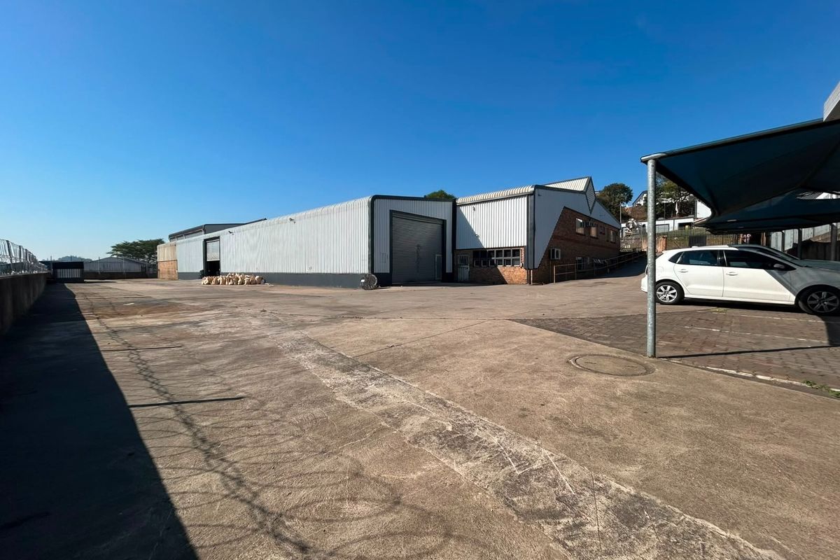 Rear exterior view of a commercial warehouse facility featuring a large concrete yard, roller shutter access, and covered parking bays.
