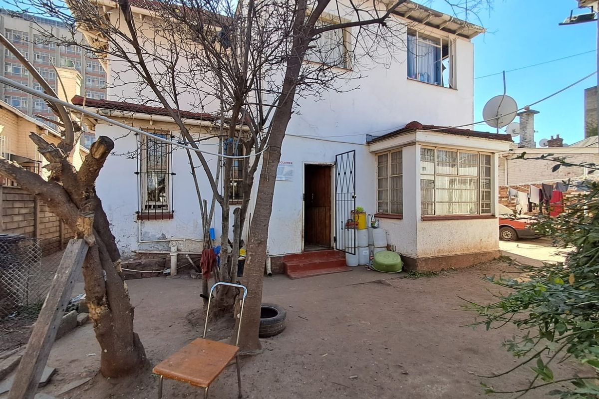 Rear view of a two-story residential property featuring plastered walls, security bars on windows, and a small enclosed sunroom area.