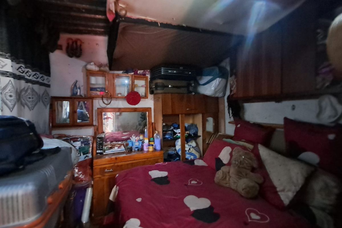 A compact bedroom featuring built-in wooden cabinetry and an exposed ceiling structure, requiring significant maintenance and cosmetic updates to improve its overall condition.
