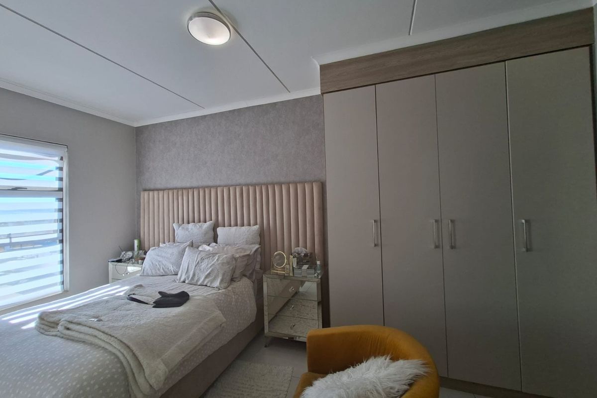 A well-maintained bedroom featuring a large built-in wardrobe, neutral wall finishes, and a modern ceiling light fixture.