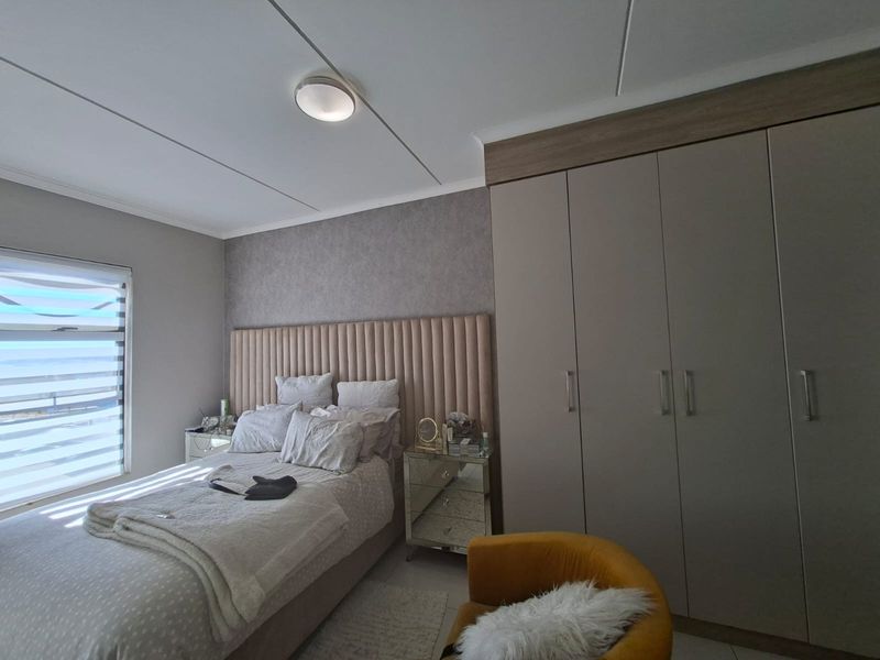 A well-maintained bedroom featuring a large built-in wardrobe, a modern upholstered headboard, and roller blinds for privacy.