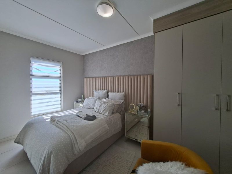 A well-maintained bedroom featuring neutral tones, built-in wardrobes, tiled flooring, and a modern ceiling light fixture with natural light from the window.
