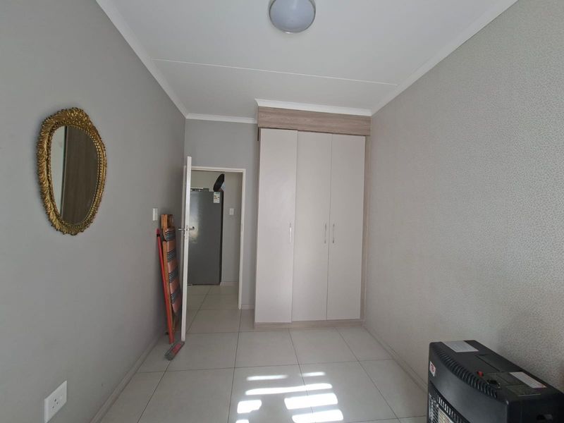 A clean, neutral bedroom featuring tiled flooring and a built-in wardrobe, offering a functional and well-maintained space.