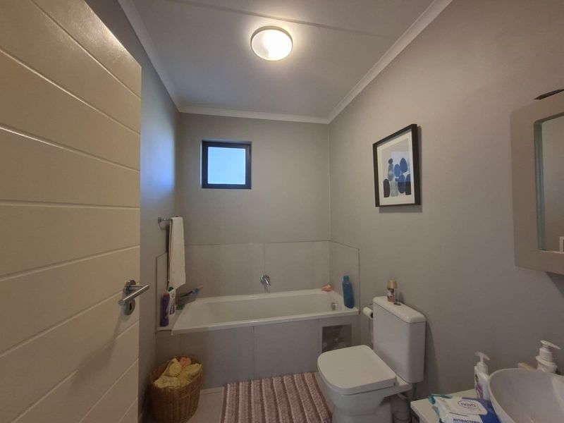 A functional bathroom featuring a built-in bathtub, toilet, and vanity basin with neutral wall finishes and tiled splashback areas.