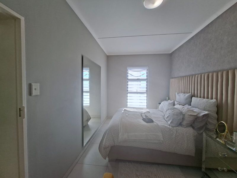 A well-maintained bedroom featuring neutral tones, a large wall-mounted mirror, tiled flooring, and a custom upholstered headboard.