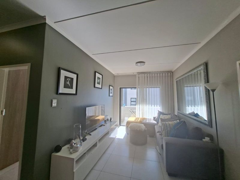 A well-maintained living room featuring tiled flooring, neutral wall tones, and a sliding glass door providing access to an outdoor balcony area.