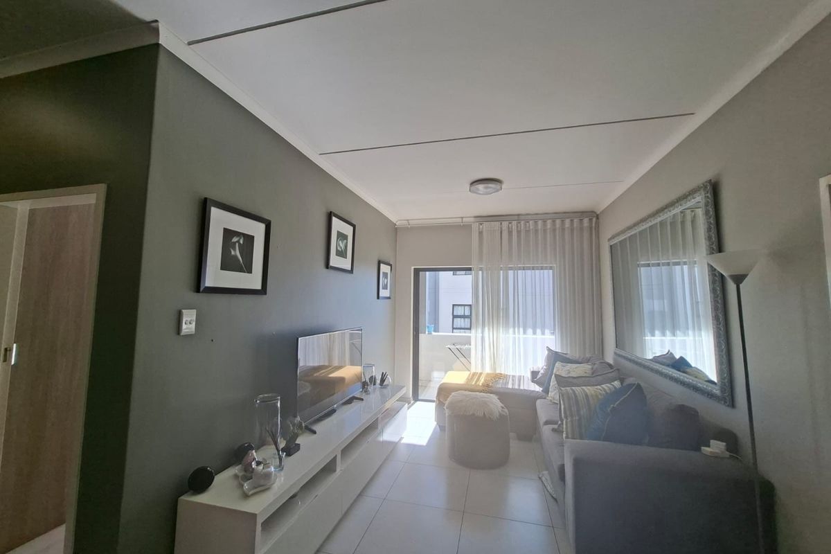 A well-maintained living room featuring tiled flooring, neutral wall tones, and a sliding glass door providing access to an outdoor balcony area.