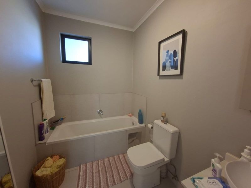 A functional bathroom featuring a built-in bathtub, toilet, and vanity basin with neutral wall finishes and tiled splashback areas.