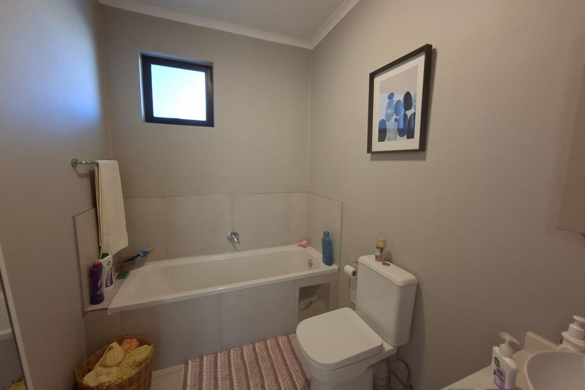 A functional bathroom featuring a built-in bathtub, toilet, and vanity basin with neutral wall finishes and tiled splashback areas.