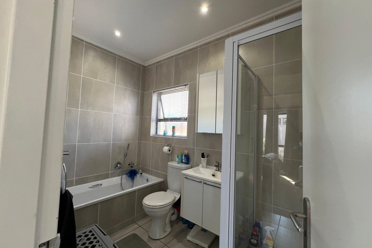 A well-maintained bathroom featuring a bathtub, separate shower enclosure, vanity unit with basin, and neutral wall and floor tiling.