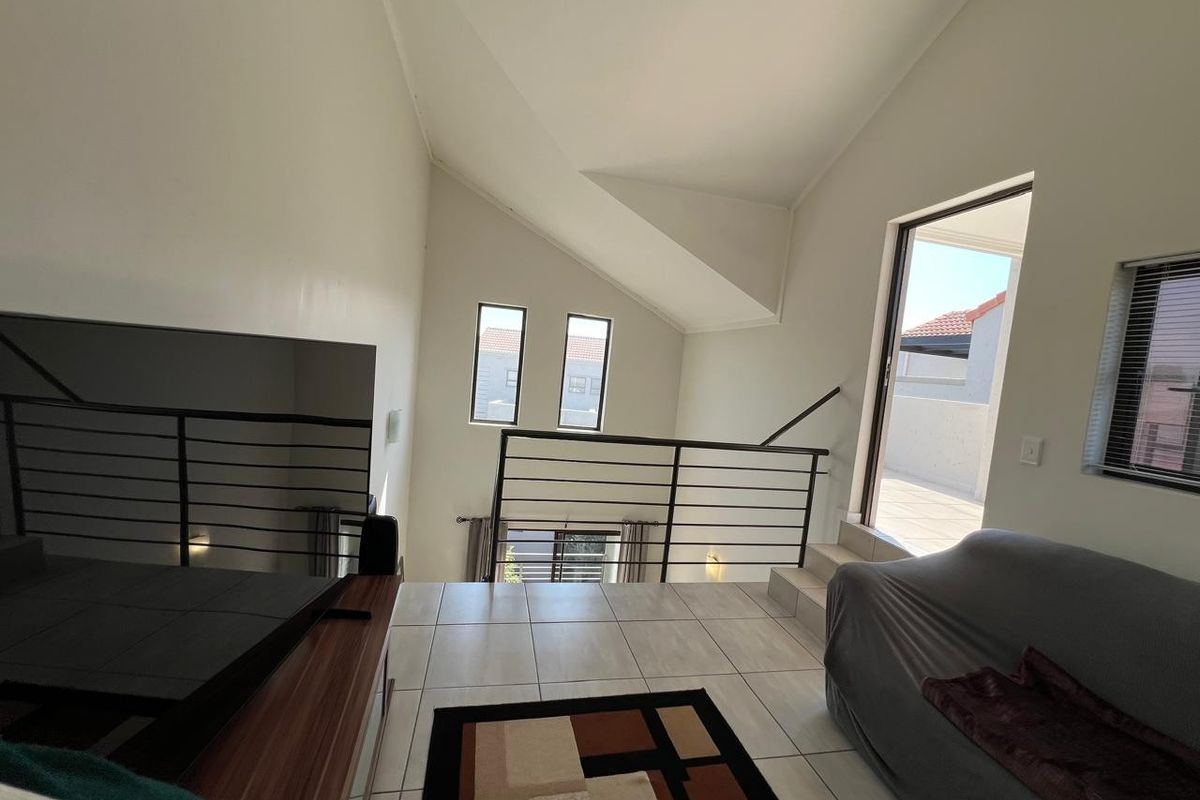Spacious living area featuring vaulted ceilings, tiled flooring, and a metal balustrade, with direct access to an outdoor balcony area.