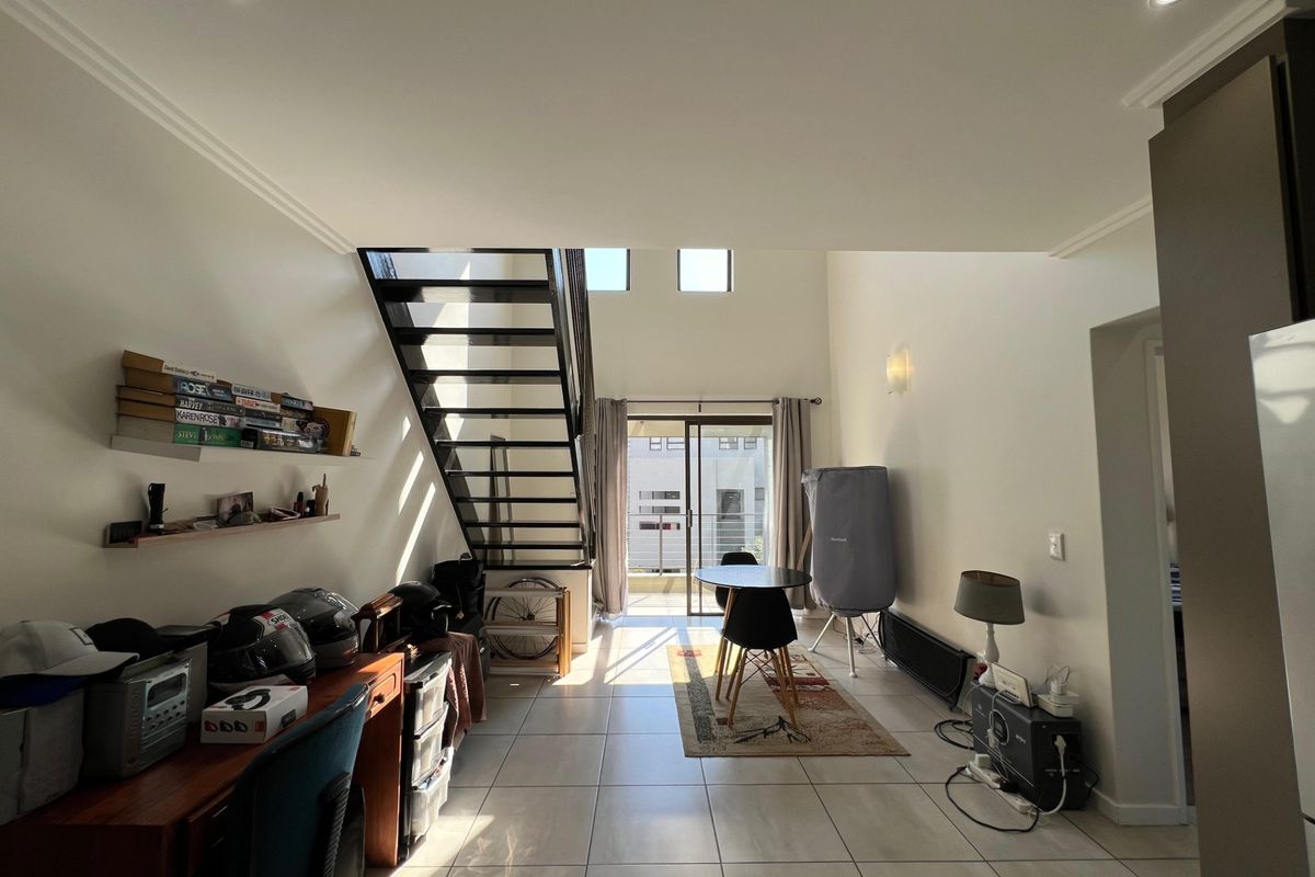 Open-plan living area featuring tiled floors, a modern metal staircase, and direct access to a balcony through sliding glass doors.