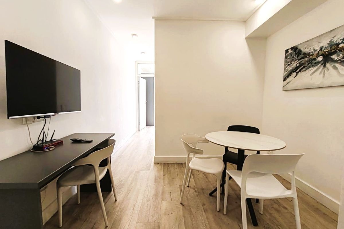 A bright living area featuring modern laminate wood flooring, recessed downlighting, and clean white walls, providing a versatile space for dining or relaxation.