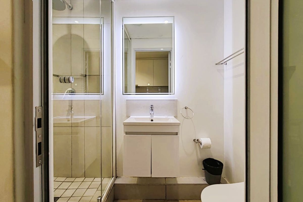 A modern, well-maintained bathroom featuring a glass-enclosed shower, wall-mounted vanity with basin, and a backlit mirror.