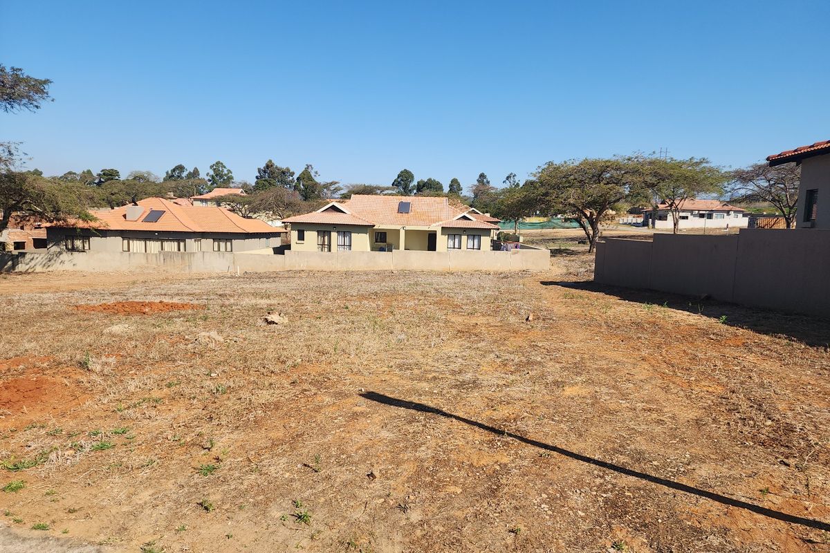 A vacant residential plot of land featuring dry vegetation and perimeter boundary walls, situated in a developed suburban neighborhood.